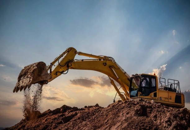 a yellow excavator digging a dirt mound